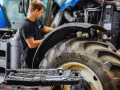Mechanik sprawdza poziom płynów eksploatacyjnych w traktorze, obok leży zestaw kluczy.