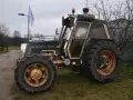 Ciemny traktor SWED-TRAC z pomarańczowymi światłami ostrzegawczymi i dużymi kołami stoi na trawie.