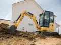 Żółta koparka gąsienicowa Caterpillar 302 CR pracuje na budowie domu, kopiąc ziemię.