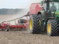 Zielony traktor z siewnikiem Horsch pracuje na polu. Trwa czas orki 1 ha, widać kurz unoszący się z ziemi.