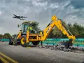 Żółta koparka JCB pracuje na drodze, a nad nią przelatuje samolot. Ciekawe, ile pali koparka, gdy pracuje tak wydajnie.