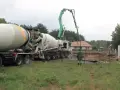 Betoniarka z wysięgnikiem pompuje beton. Pracownik w zielonej kurtce obserwuje. To ważny etap budowy, a czyszczenie betoniarki po pracy, jak usunąć zaschnięty beton z betoniarki, jest kluczowe.