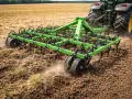 Zielony kultywator z zębami spulchnia ziemię na polu, przygotowując ją do siewu. To narzędzie rolnicze, które pomaga w uprawie.