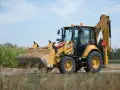 Żółta koparko-ładowarka CAT 432 w trakcie budowy drogi, z pełną łyżką ziemi.