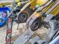 Naprawa tulejowania koparki. Widoczne elementy hydrauliczne i zardzewiałe sworznie.