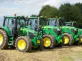Rząd zielonych traktorów John Deere z żółtymi felgami na polu. Widać ich charakterystyczny wygląd i potężne opony.