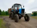 Niebieski traktor z przyczepą na tle wiejskiego krajobrazu. Zastanawiasz się, ile zarabia traktorzysta?