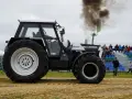Ciężki traktor Ursus 1224 z potężnym dymem z rury wydechowej podczas zawodów tractor pulling. Widownia obserwuje z trybun.