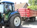 Operator traktora w czerwonej koszulce prowadzi maszynę z przyczepą.