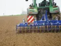 Zielony traktor z agregatem uprawowym, który przygotowuje pole. Różne rodzaje wałów uprawowych pomagają w tym procesie.