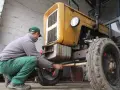 Mężczyzna w zielonych spodniach i czapce reguluje przednie koło żółtego ciągnika 4x4, pokazując, jak ustawić zbieżność.