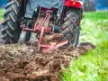 Czerwony traktor z pługiem orze pole, przygotowując ziemię pod zasiew. Rolnictwo w akcji.