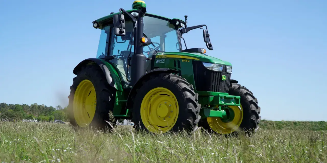 Zielony traktor John Deere 5095 M, z mocą 100km, gotowy do pracy na polu.