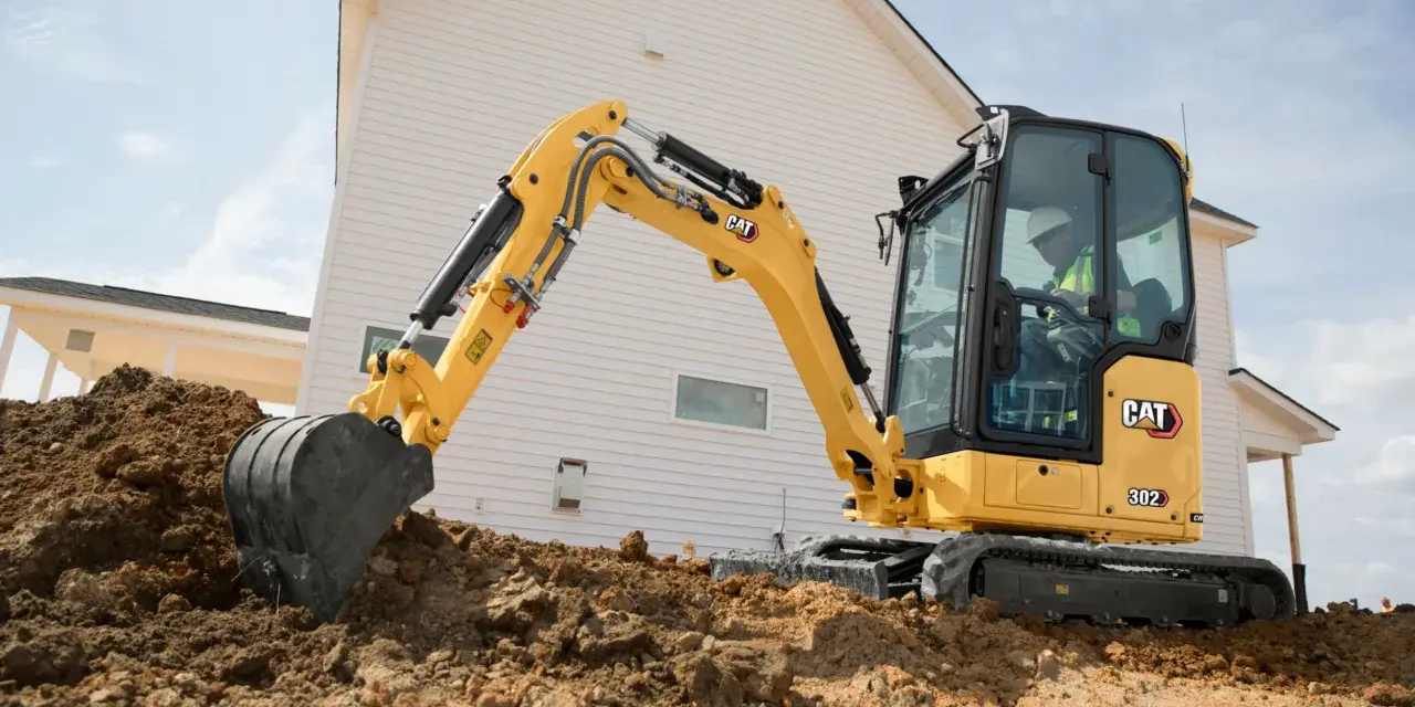 Żółta koparka gąsienicowa Caterpillar 302 CR pracuje na budowie domu, kopiąc ziemię.