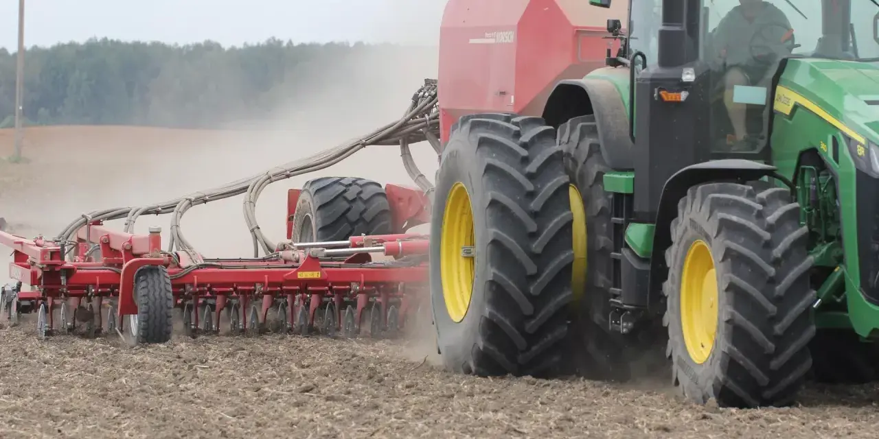 Zielony traktor z siewnikiem Horsch pracuje na polu. Trwa czas orki 1 ha, widać kurz unoszący się z ziemi.