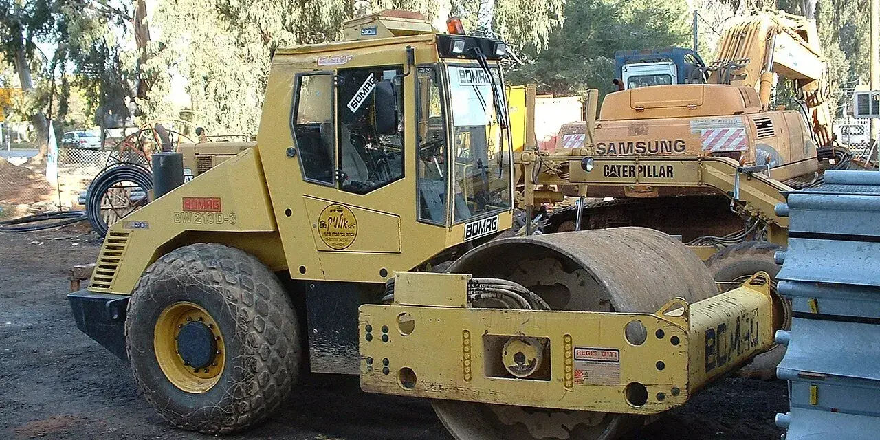Żółty walec drogowy BOMAG BW 213D-3 gotowy do budowy drogi. W tle koparka Samsung Caterpillar.