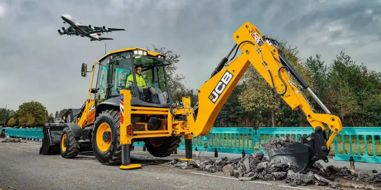Żółta koparka JCB pracuje na drodze, a nad nią przelatuje samolot. Ciekawe, ile pali koparka, gdy pracuje tak wydajnie.