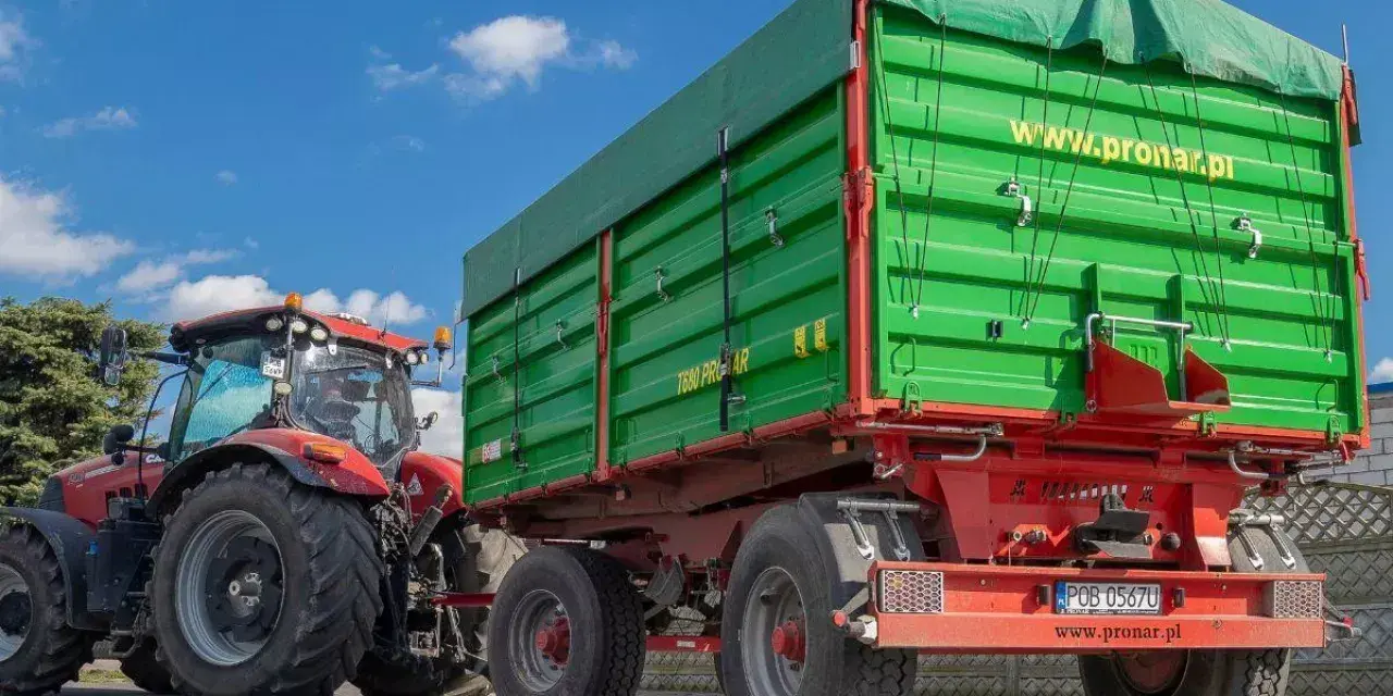 Czerwony traktor z zieloną przyczepą rolniczą. Czy przyczepa rolnicza musi być zarejestrowana? Sprawdź przepisy!