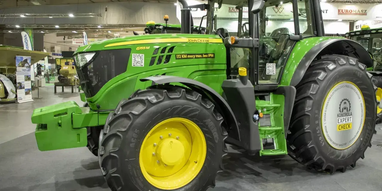 Zielony traktor marki John Deere 6155 M, gotowy do pracy na polu.