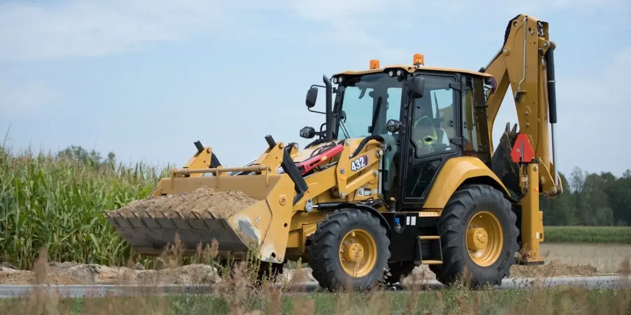 Żółta koparko-ładowarka CAT 432 w trakcie budowy drogi, z pełną łyżką ziemi.
