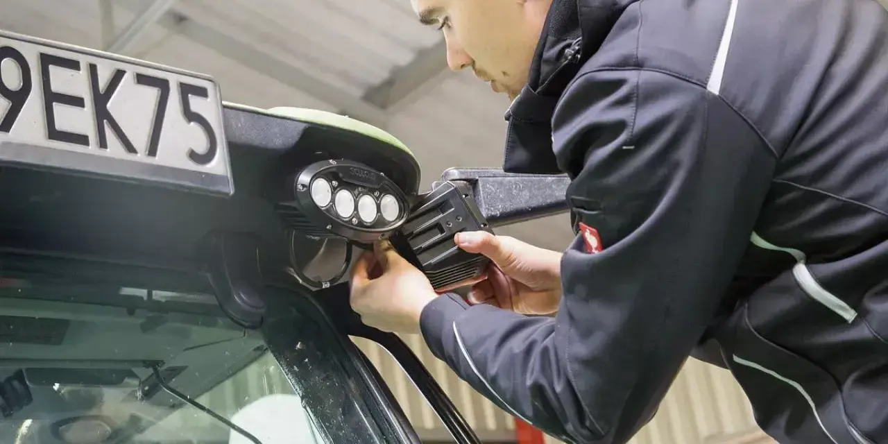 Mężczyzna montuje lampy LED na ciągniku. Dowiedz się, jak podłączyć lampy LED w ciągniku, aby poprawić widoczność w nocy.