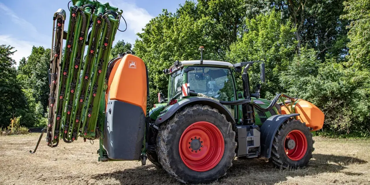 Zielony traktor z zamontowanym opryskiwaczem polowym, gotowy do pracy.