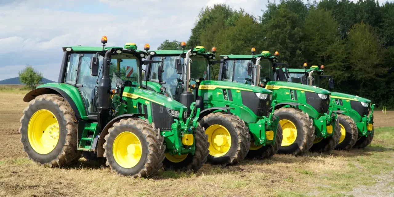 Rząd zielonych traktorów John Deere z żółtymi felgami na polu. Widać ich charakterystyczny wygląd i potężne opony.