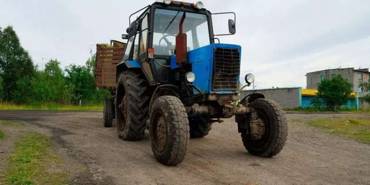Niebieski traktor z przyczepą na tle wiejskiego krajobrazu. Zastanawiasz się, ile zarabia traktorzysta?