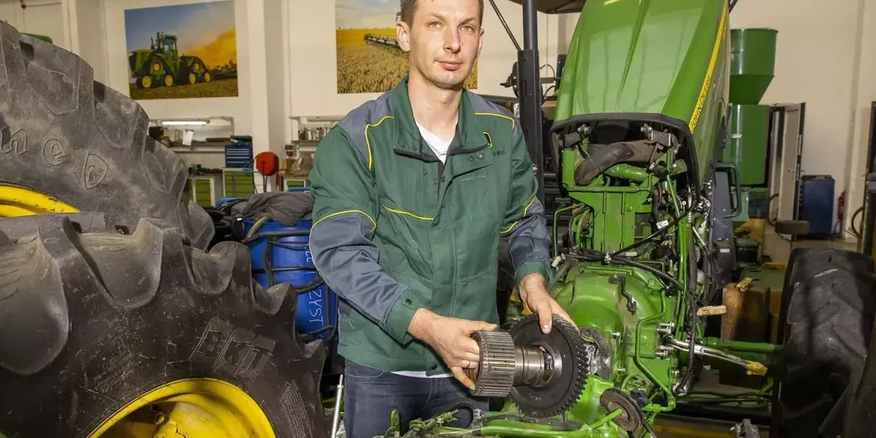 Mechanik z częścią John Deere, być może szuka informacji o john deere kody serwisowe, aby naprawić traktor.