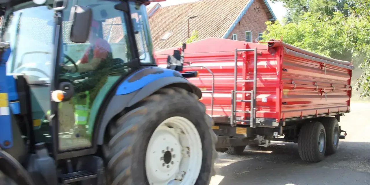 Operator traktora w czerwonej koszulce prowadzi maszynę z przyczepą.