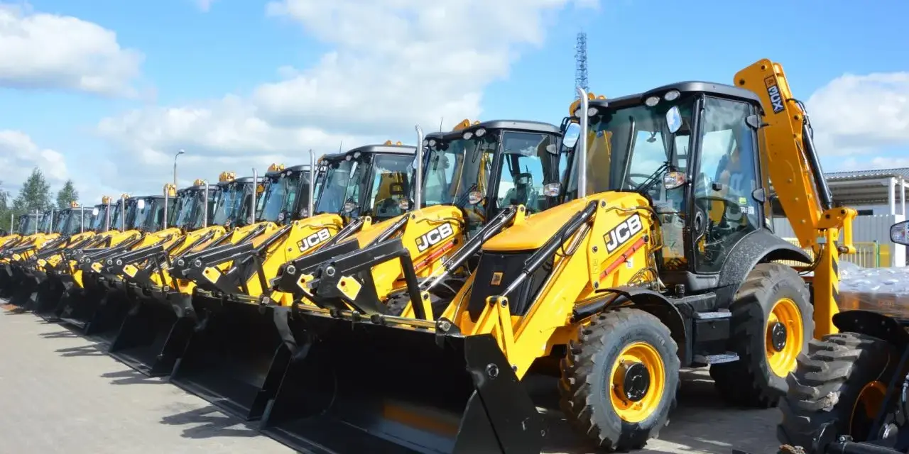 Rząd żółtych koparko-ładowarek JCB stoi na placu.