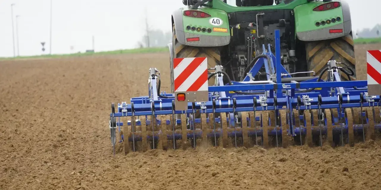 Zielony traktor z agregatem uprawowym, który przygotowuje pole. Różne rodzaje wałów uprawowych pomagają w tym procesie.
