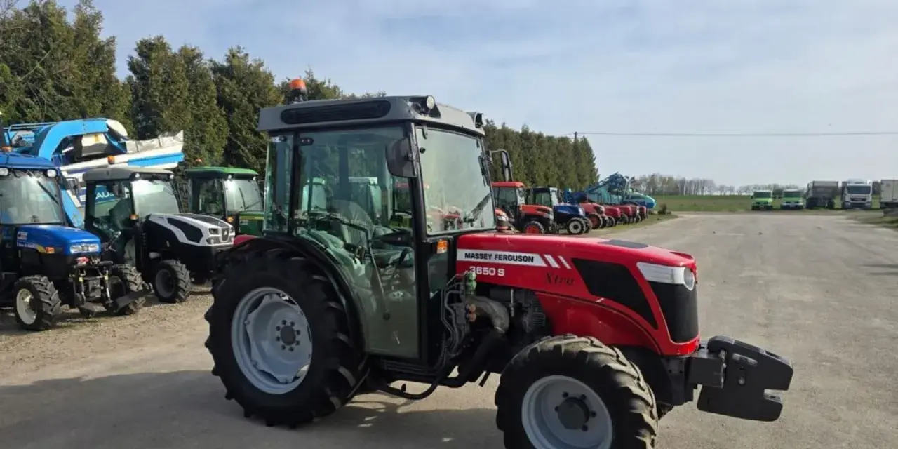 Czerwony ciągnik Massey Ferguson 3650 S Xtra, z kabiną, zaparkowany na placu z innymi maszynami. Dane techniczne tego modelu są imponujące.