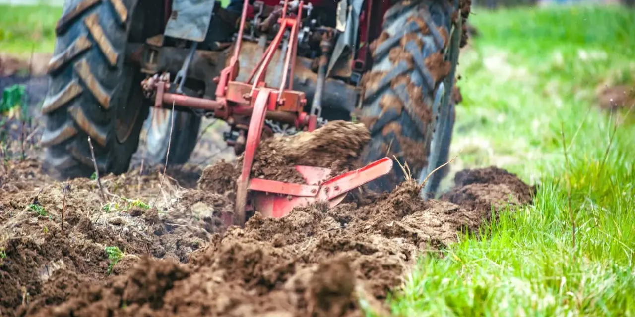 Czerwony traktor z pługiem orze pole, przygotowując ziemię pod zasiew. Rolnictwo w akcji.