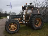 Ciemny traktor SWED-TRAC z pomarańczowymi światłami ostrzegawczymi i dużymi kołami stoi na trawie.