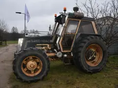 Ciemny traktor SWED-TRAC z pomarańczowymi światłami ostrzegawczymi i dużymi kołami stoi na trawie.