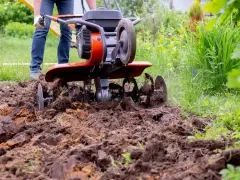 Mężczyzna pracuje glebogryzarką samoróbką, spulchniając ziemię w ogrodzie.