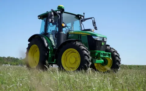 Zielony traktor John Deere 5095 M, z mocą 100km, gotowy do pracy na polu.