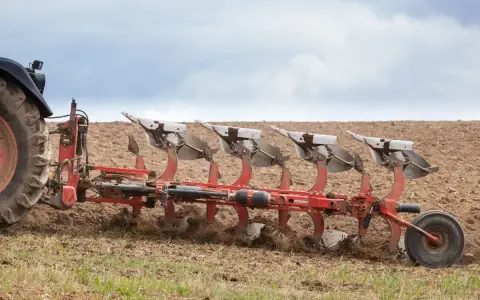 Ciągnik z pługiem orze pole. Widać pracujące lemiesze, które odwracają ziemię. Prędkość orki jest optymalna dla tej maszyny.