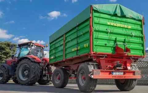Czerwony traktor z zieloną przyczepą rolniczą. Czy przyczepa rolnicza musi być zarejestrowana? Sprawdź przepisy!