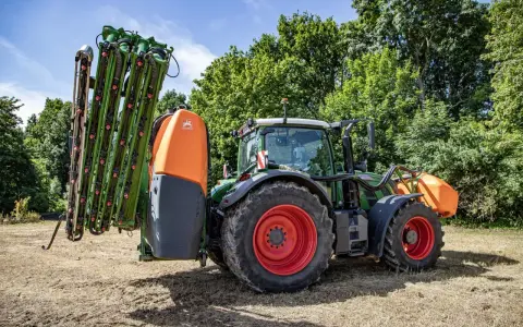 Zielony traktor z zamontowanym opryskiwaczem polowym, gotowy do pracy.