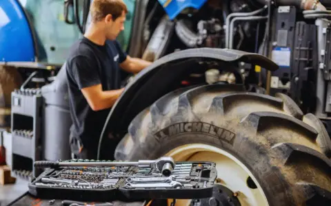 Mechanik pracuje przy traktorze, a obok leży walizka z narzędziami. Kluczowe dla sprawnej konserwacji maszyn rolniczych są regularne przeglądy.