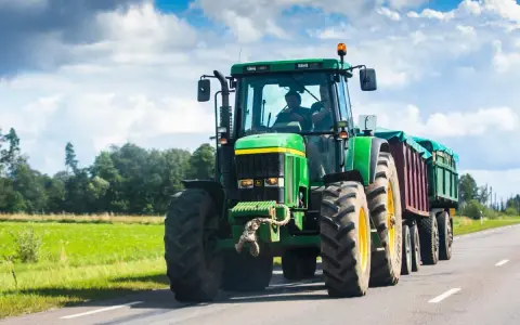 Zielony traktor z przyczepą jedzie po drodze. Zastanawiasz się, ile pali traktor?