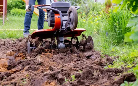 Mężczyzna pracuje glebogryzarką samoróbką, spulchniając ziemię w ogrodzie.