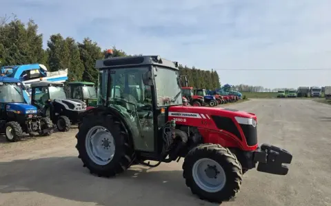 Czerwony ciągnik Massey Ferguson 3650 S Xtra, z kabiną, zaparkowany na placu z innymi maszynami. Dane techniczne tego modelu są imponujące.