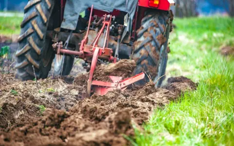Czerwony traktor z pługiem orze pole, przygotowując ziemię pod zasiew. Rolnictwo w akcji.