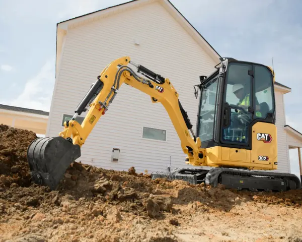 Żółta koparka gąsienicowa Caterpillar 302 CR pracuje na budowie domu, kopiąc ziemię.