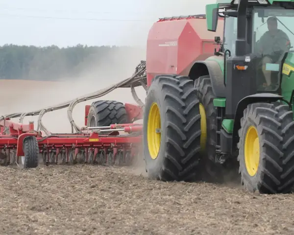 Zielony traktor z siewnikiem Horsch pracuje na polu. Trwa czas orki 1 ha, widać kurz unoszący się z ziemi.