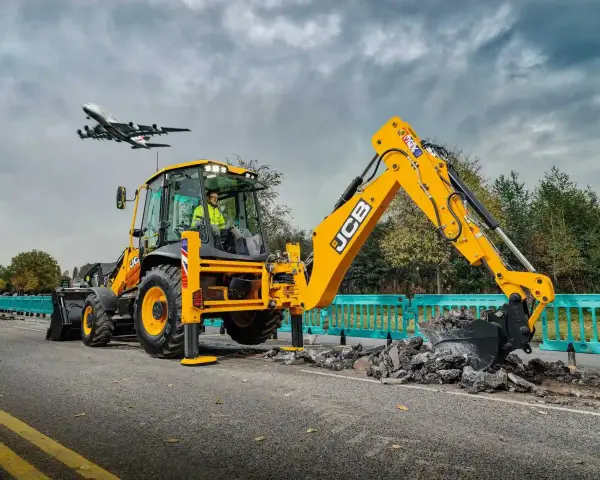 Żółta koparka JCB pracuje na drodze, a nad nią przelatuje samolot. Ciekawe, ile pali koparka, gdy pracuje tak wydajnie.