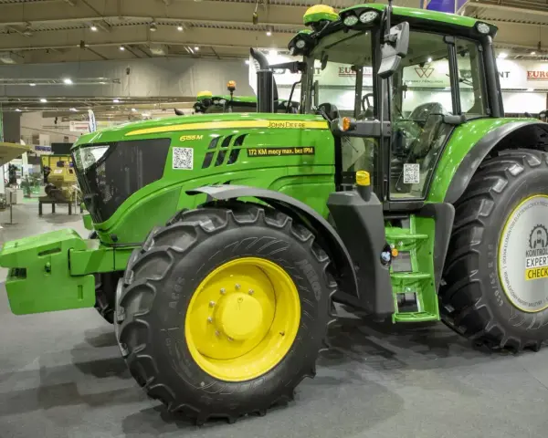 Zielony traktor marki John Deere 6155 M, gotowy do pracy na polu.